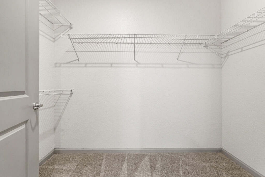Empty closet with white wire shelves on three walls, beige carpeted floor, and white door partially open on the left side.